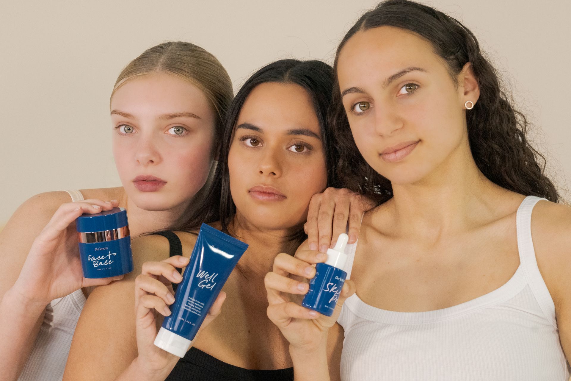 Three women pose holding blue skincare products against a light background.