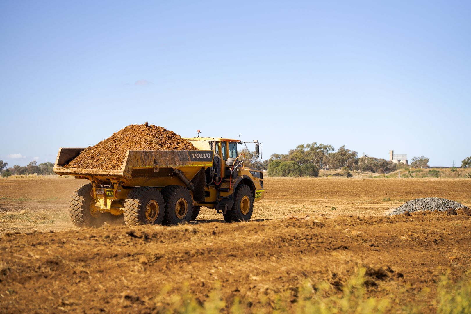 Yellow dump truck loaded with dirt at a construction site under a clear blue sky