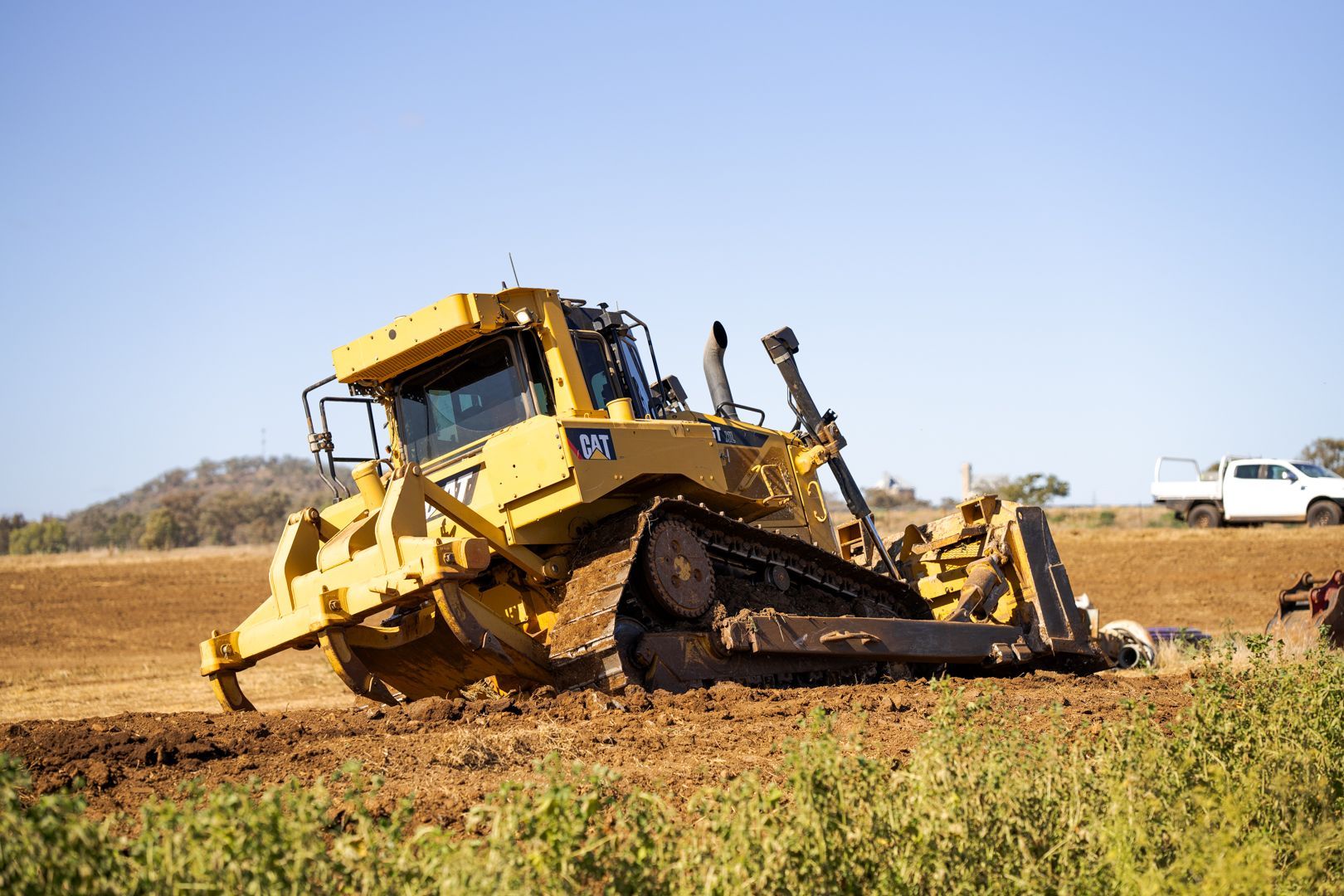 Yellow bulldozer moving dirt in a dry field under a clear blue sky