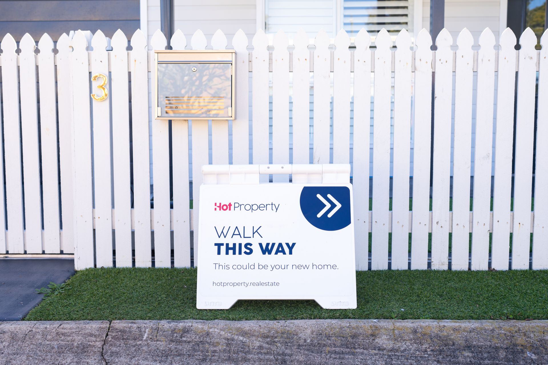 Sign directing walkers: “WALK THIS WAY” beside a white picket fence on a sidewalk.