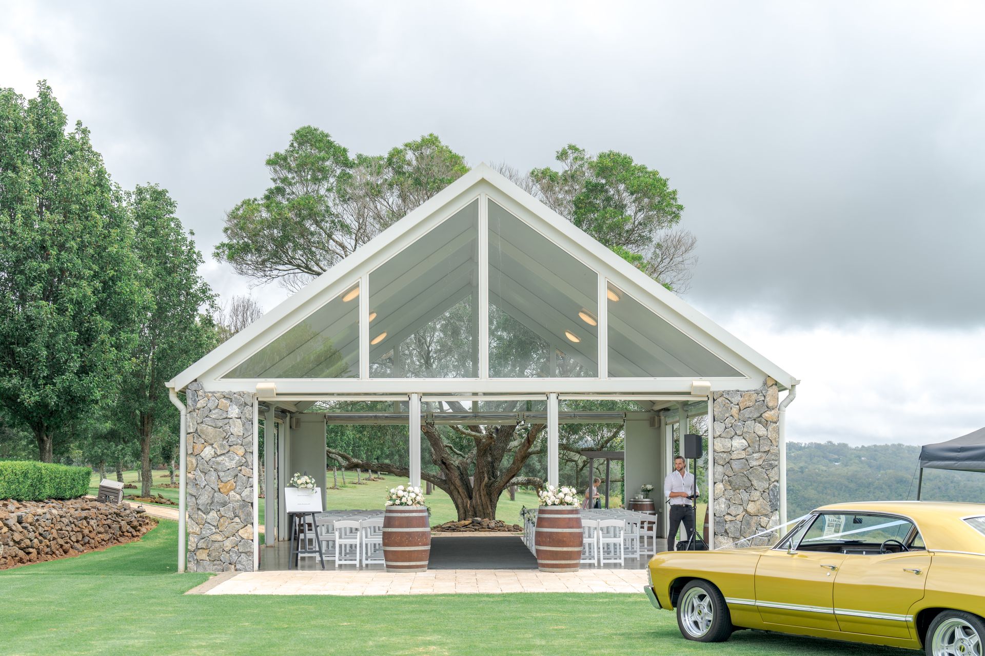 Modern glass house with stone columns and a yellow vintage car in front