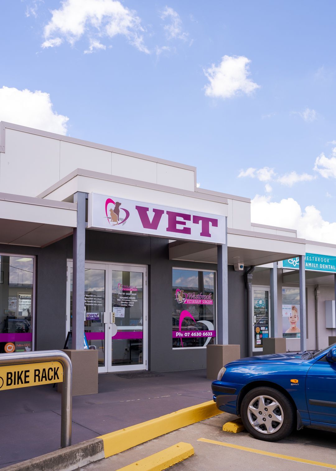 Storefront of a vet clinic with pink and white signage, next to a parked blue pickup truck.