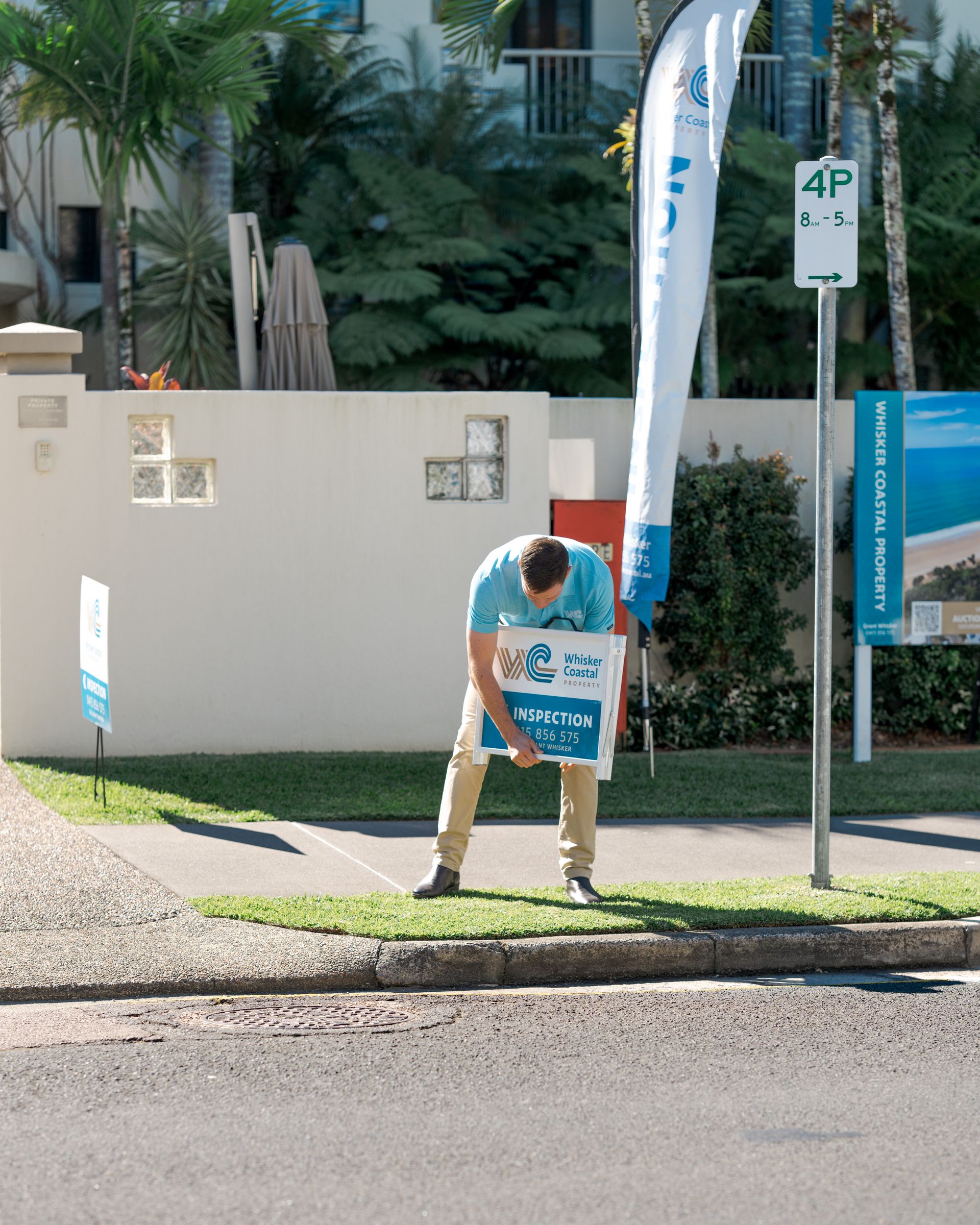 Person holding a blue sign beside a parking sign on a sunny sidewalk.