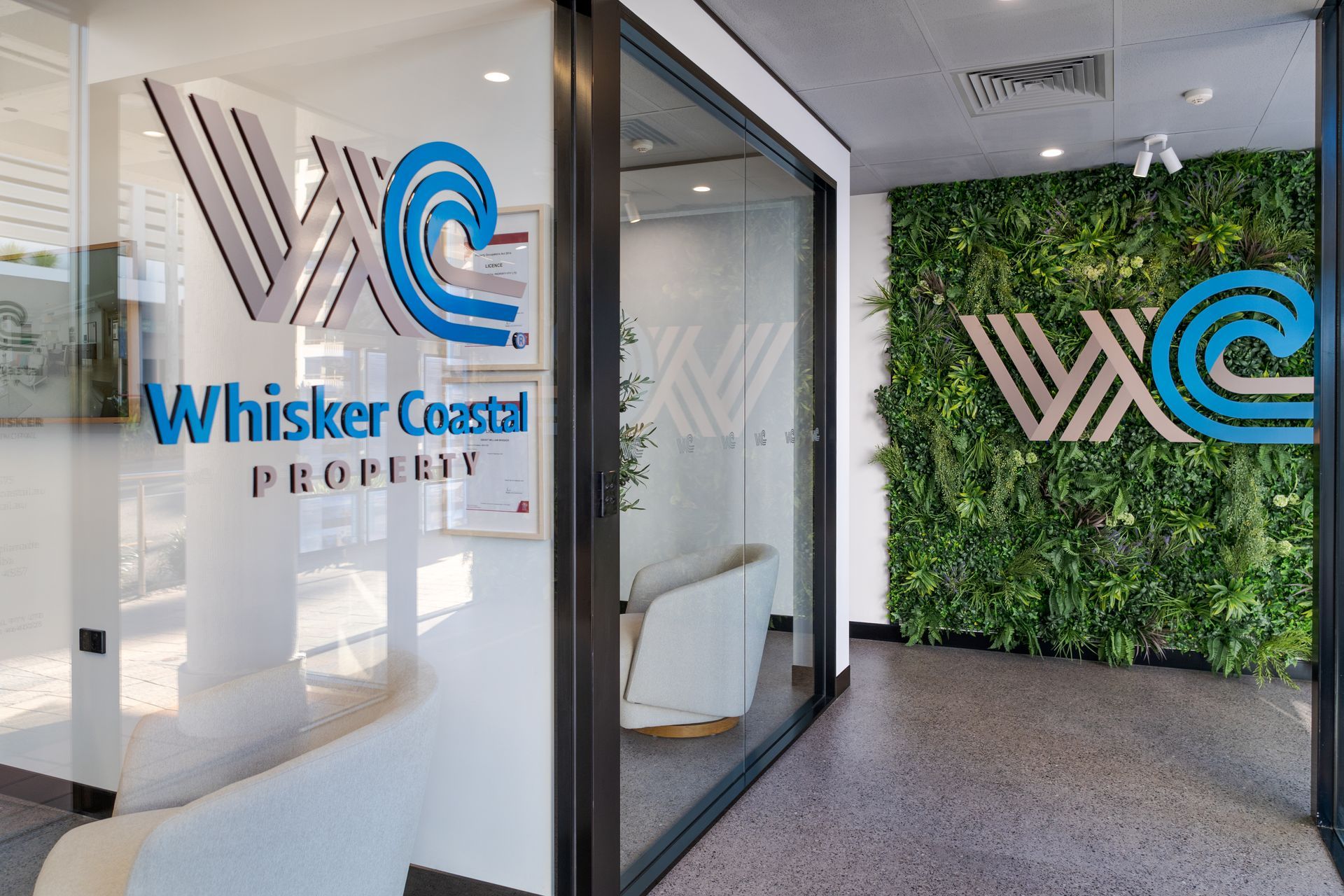 Whisker Coast Property office entrance with glass doors and logo, beside a green plant wall