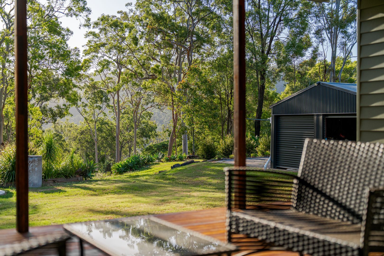 Covered patio overlooking a sunlit green garden with trees and a small shed