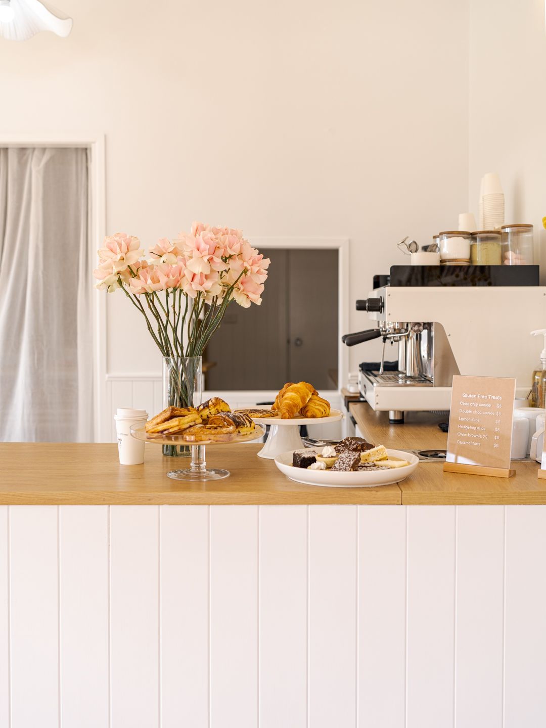 Bright kitchen counter with pastries, fruit, pink flowers, and a coffee machine