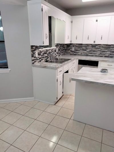 White kitchen with tile floor, cabinets, and countertops, and a gray backsplash.