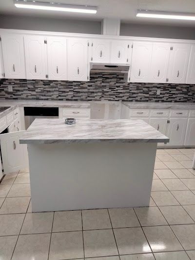 White kitchen with a countertop island and cabinets, gray backsplash, and beige tiled floor.