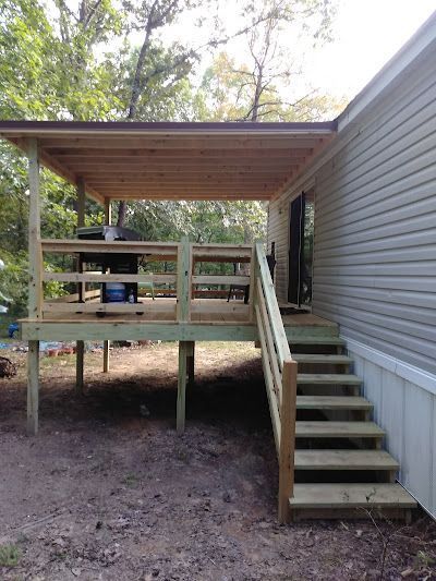 Wooden deck with a covered porch attached to a light-colored mobile home. Staircase leads up to the deck.