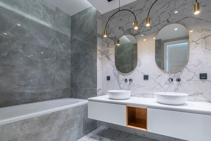 Modern bathroom with marble-look tiles, dual vanity with round sinks, oval mirrors, and hanging lights. Includes a bathtub.