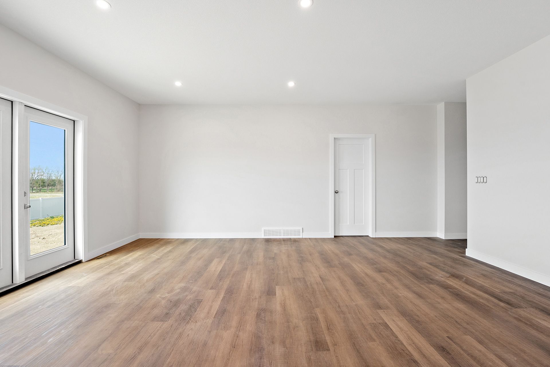 Empty room with hardwood floors, white walls, and a door to an outdoor view.