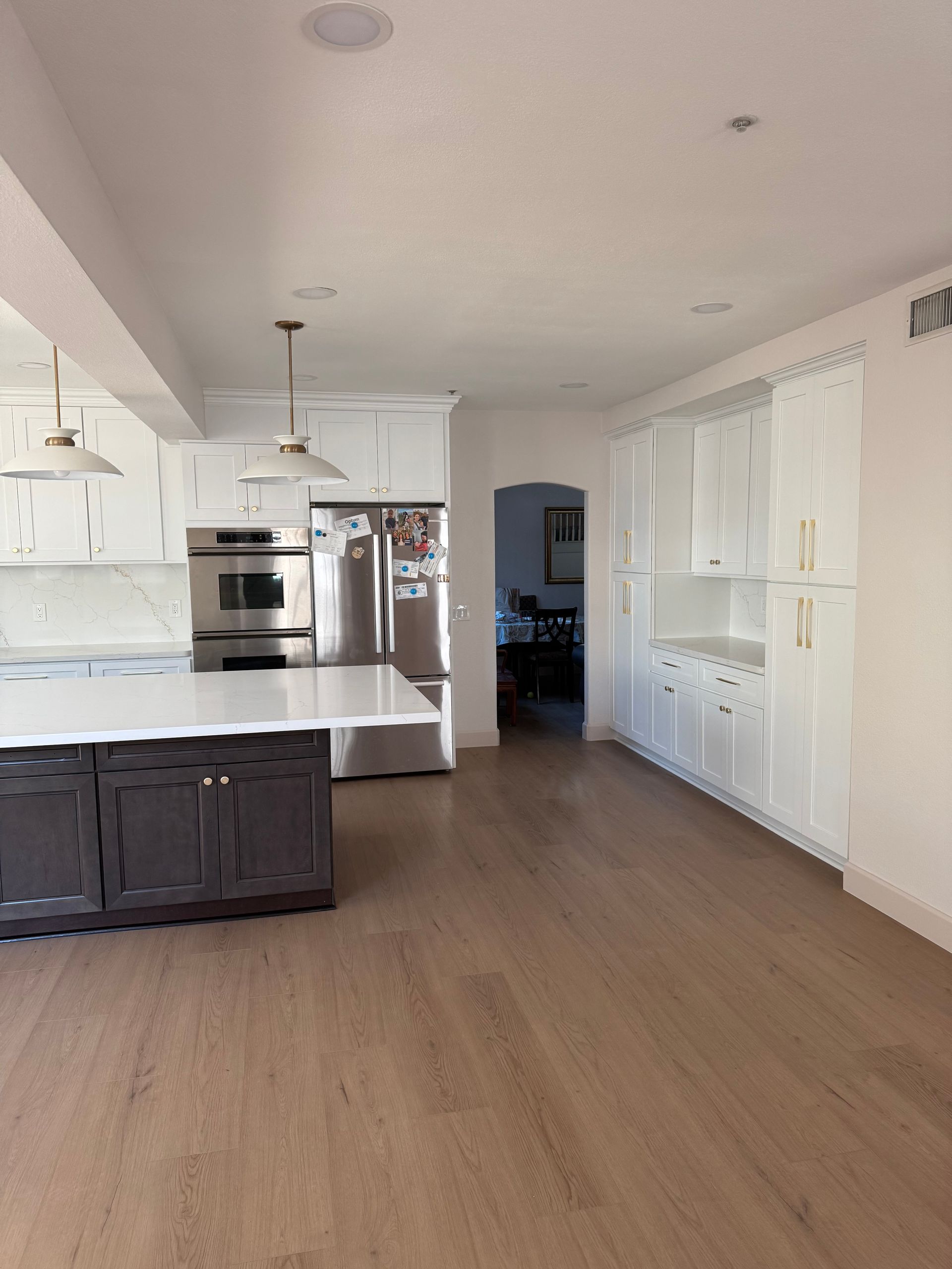 Modern kitchen with white cabinets, dark island, and stainless steel appliances. Hardwood floors and doorway to other room.