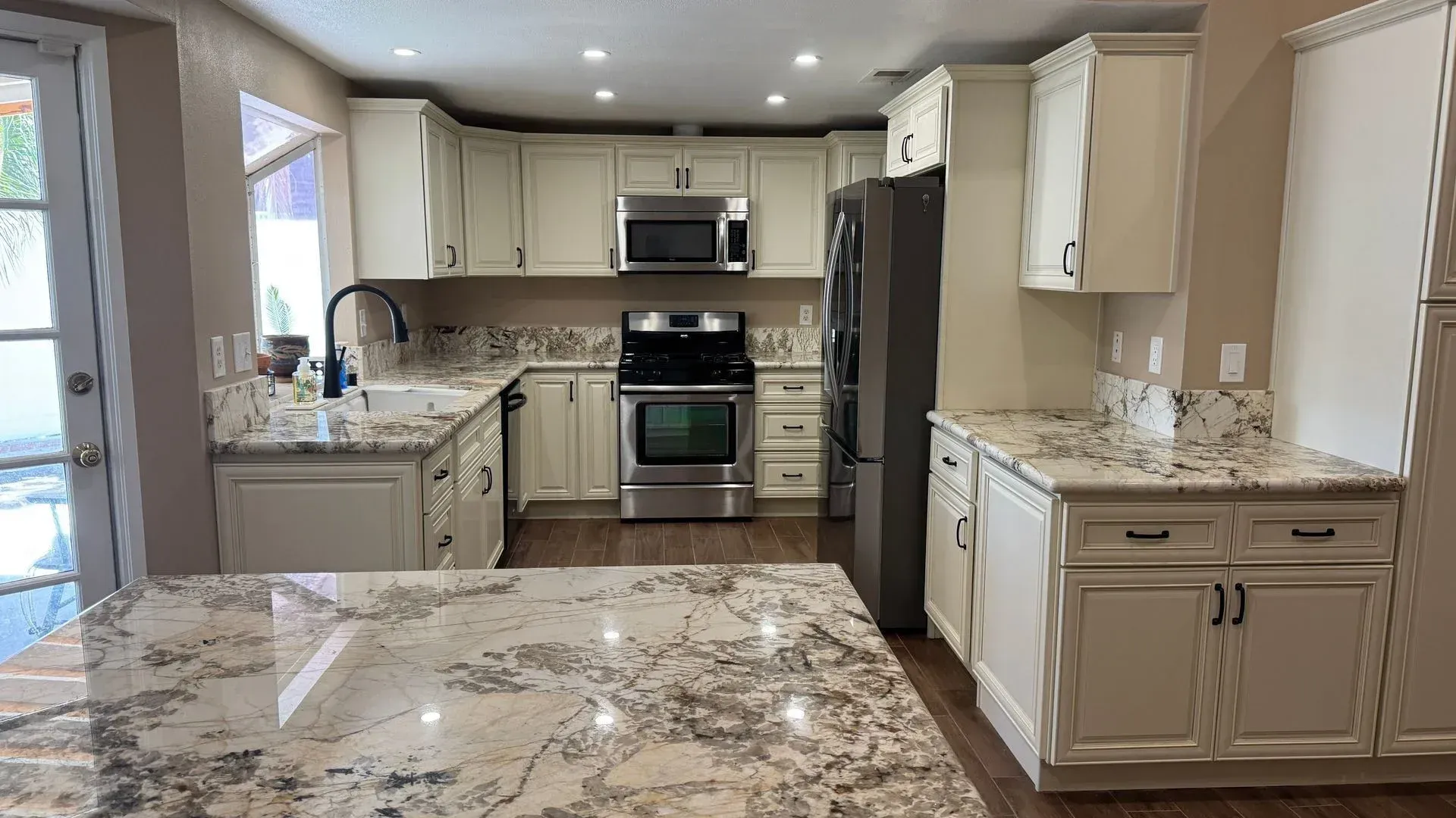 Bright modern kitchen with cream cabinets, granite countertops, stainless appliances, and tiled floor