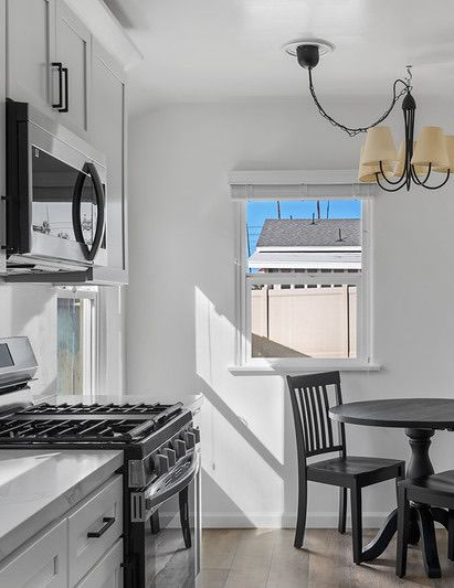 A modernized kitchen featuring white cabinetry, stainless steel appliances, and a small dining area with a black table and chairs