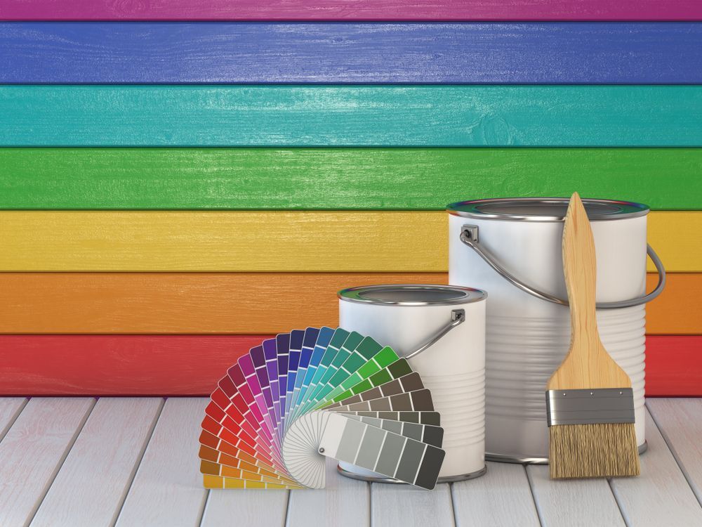 Three Cans Of Paint And A Brush Are On A Wooden Floor In Front Of A Rainbow Colored Wall — Yves De Wilde Quality Painting Services In Lismore, NSW