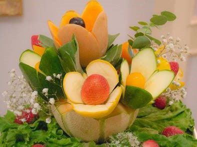 Colorful carved fruit arrangement with melon, apple, grapes, and leafy garnishes on a table