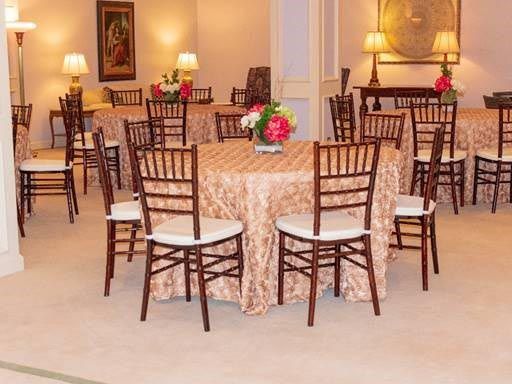 Banquet room with round tables, wooden chairs, and floral centerpieces under warm lighting