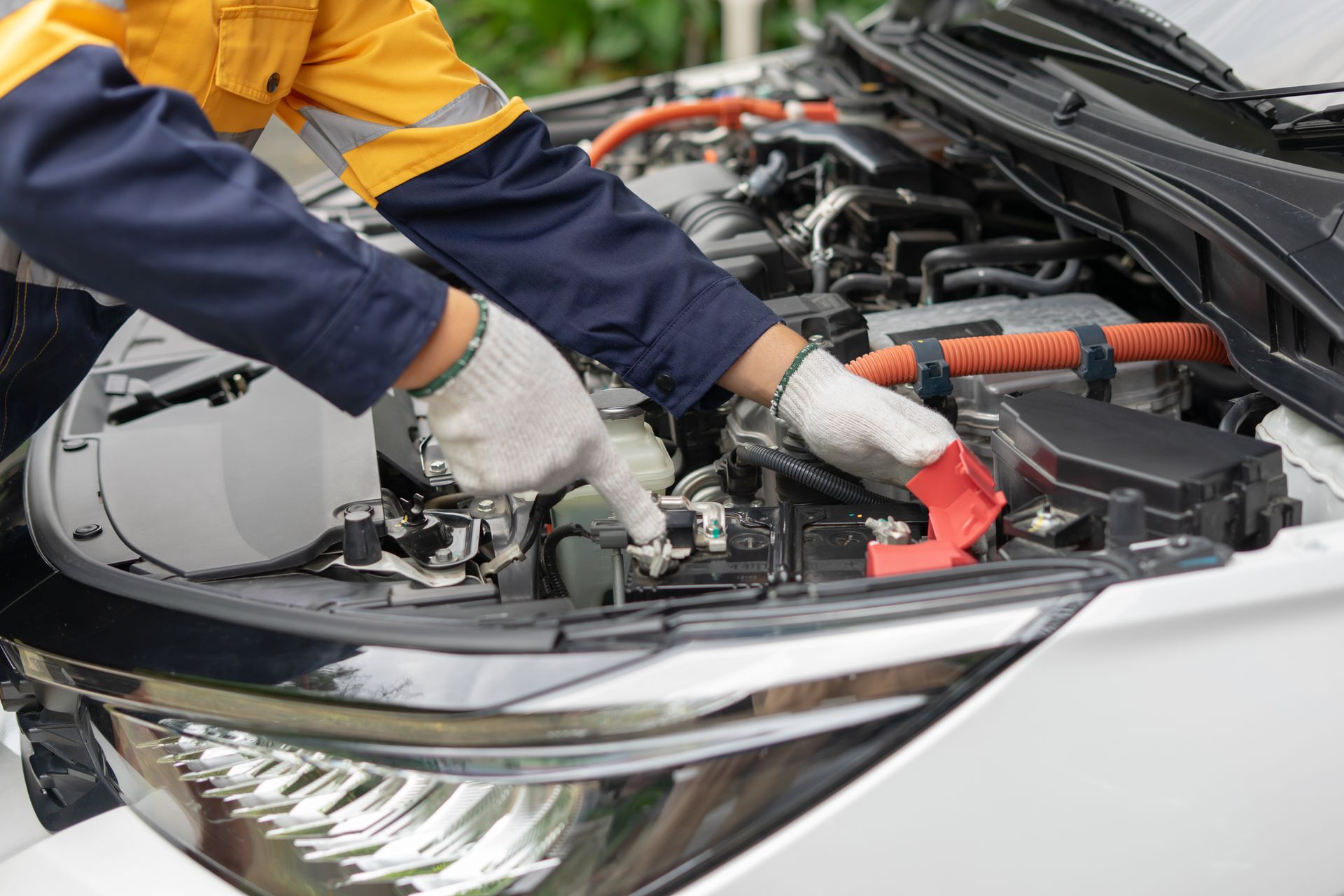 Mechanic working under a car hood with gloved hands on engine components | Spenser's Quality Automotive