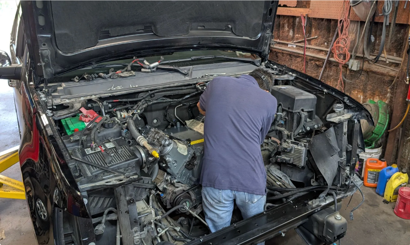 Person working on a damaged car engine in a garage, hood open and front end exposed | Spenser's Quality Automotive