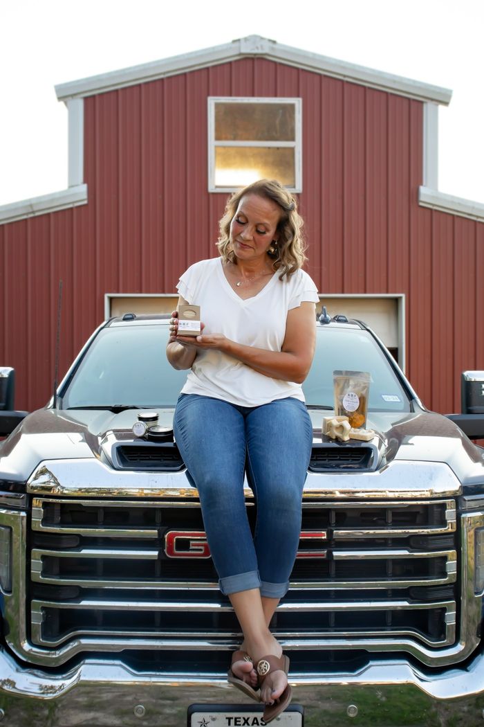 HELLO!! I'm Robyn! :) Image of Robyn Holding a goats milk soap. Sitting on truck hood