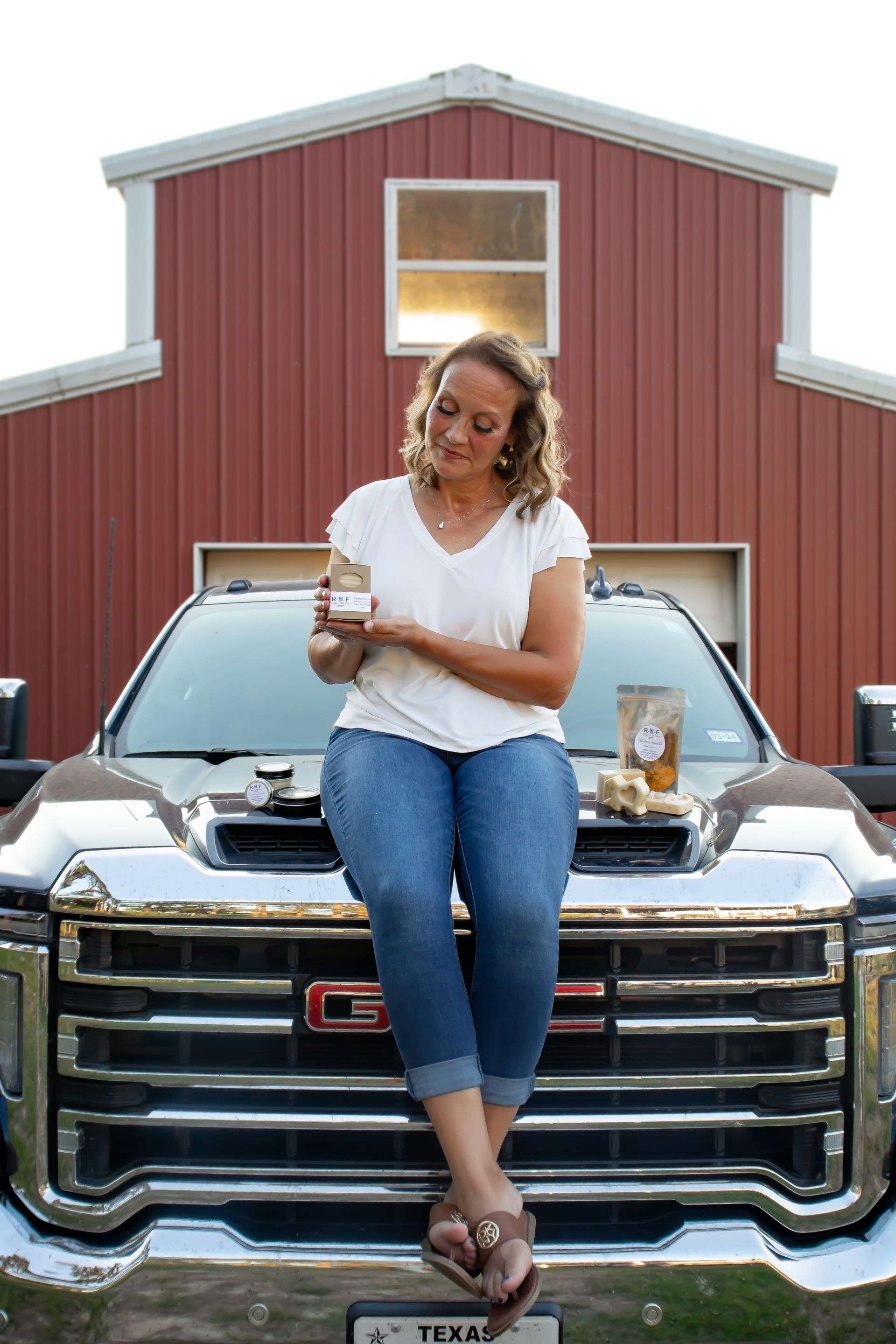 HELLO!! I'm Robyn! :) Image of Robyn Holding a goats milk soap. Sitting on truck hood