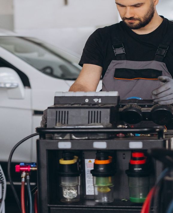 Mechanic in black apron working on a machine with clear tanks in a garage | OG Autoworks