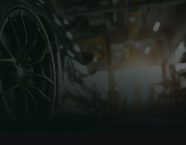 Dim industrial machinery with a large wheel in a dark, blurred factory setting | OG Autoworks