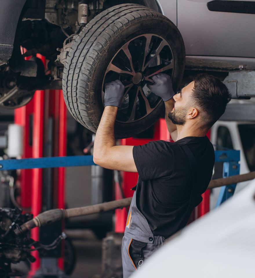 Mechanic inspecting a lifted car’s wheel in an auto repair shop | OG Autoworks