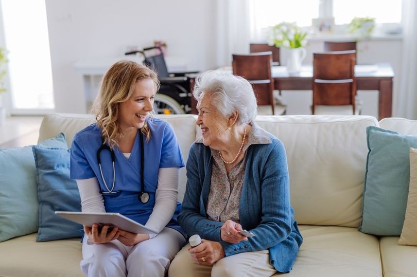 Nurse speaking with a smiling patient on a couch in a bright living room