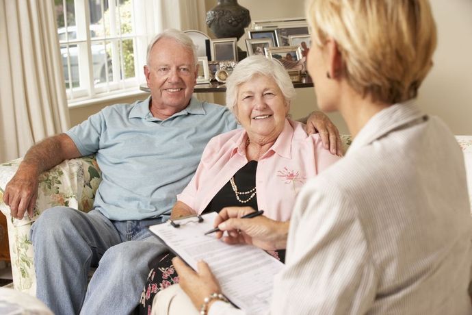 Couple speaking with a counselor in a bright living room, seated on a sofa and taking notes.