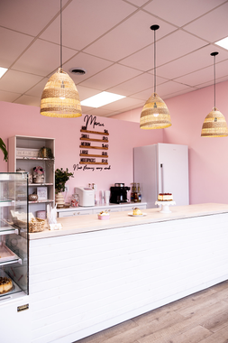 Pink café interior with white counter, hanging woven lights, and pastry display shelves