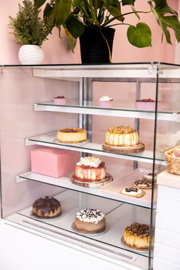 Bakery display case with assorted pastries and cakes on glass shelves, topped with potted plants