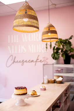Pink bakery counter with cheesecakes on a wooden table and wicker pendant lights in a pastel shop