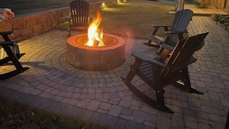 A fire pit is surrounded by rocking chairs on a patio. Greer 
