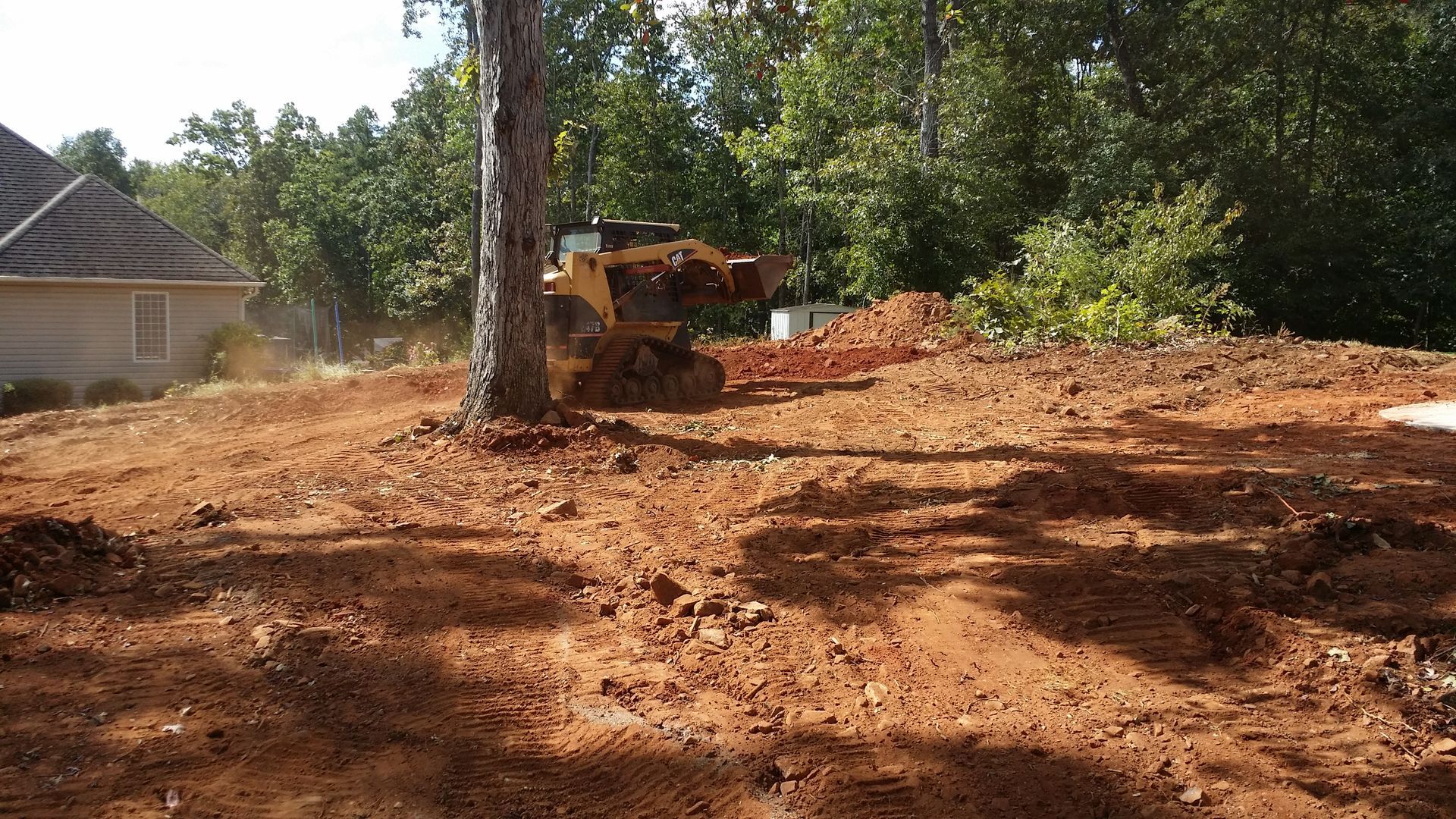 A bulldozer is working on a dirt field in front of a house mayo