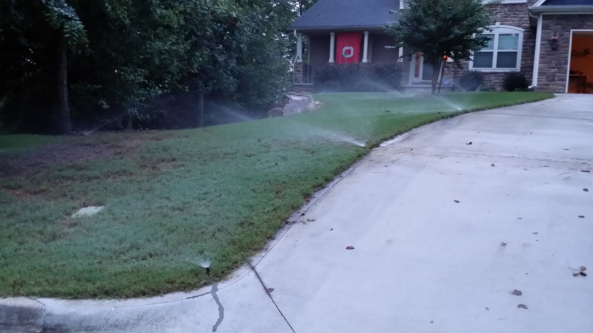 A lawn sprinkler is spraying water on a lush green lawn in front of a house.