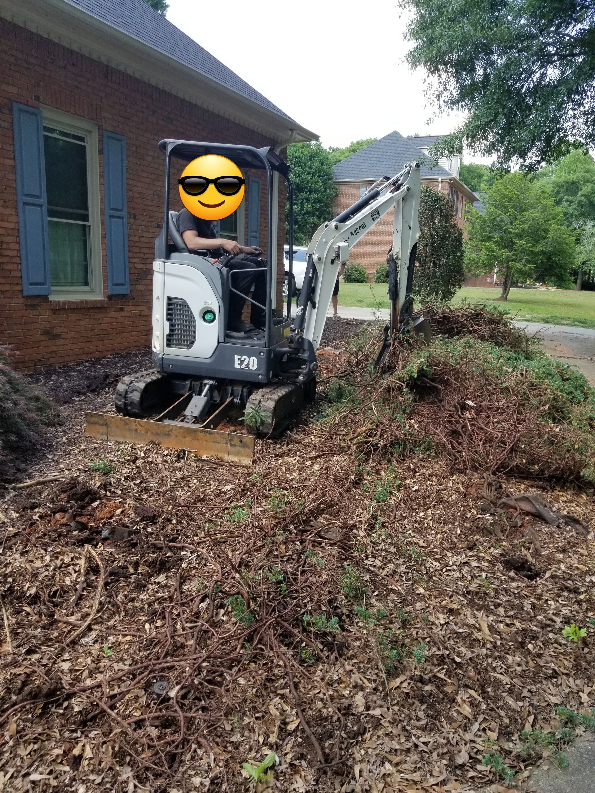 A man is driving a small excavator in front of a brick house in Lyman.