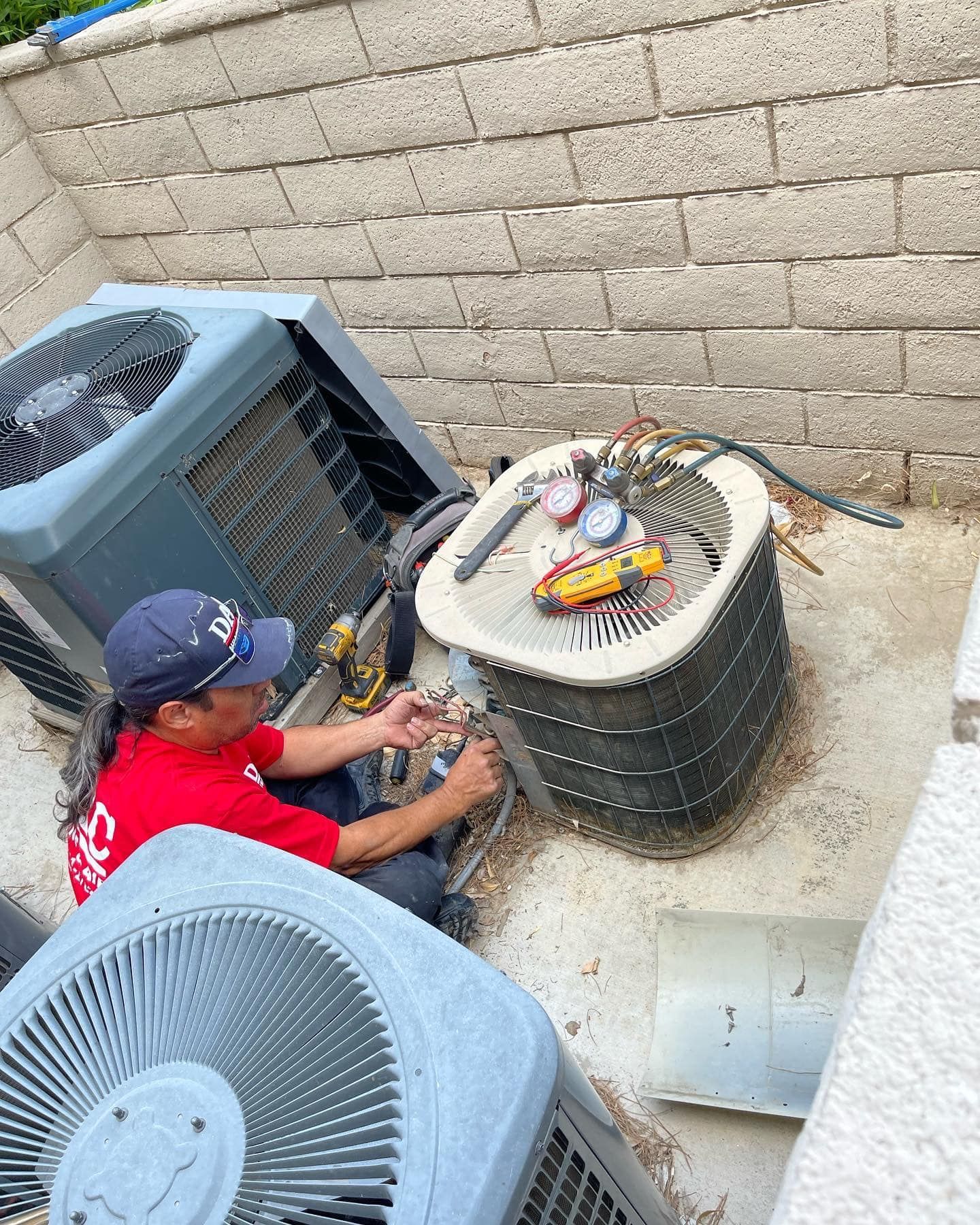 A man is sitting on the ground working on an air conditioner.