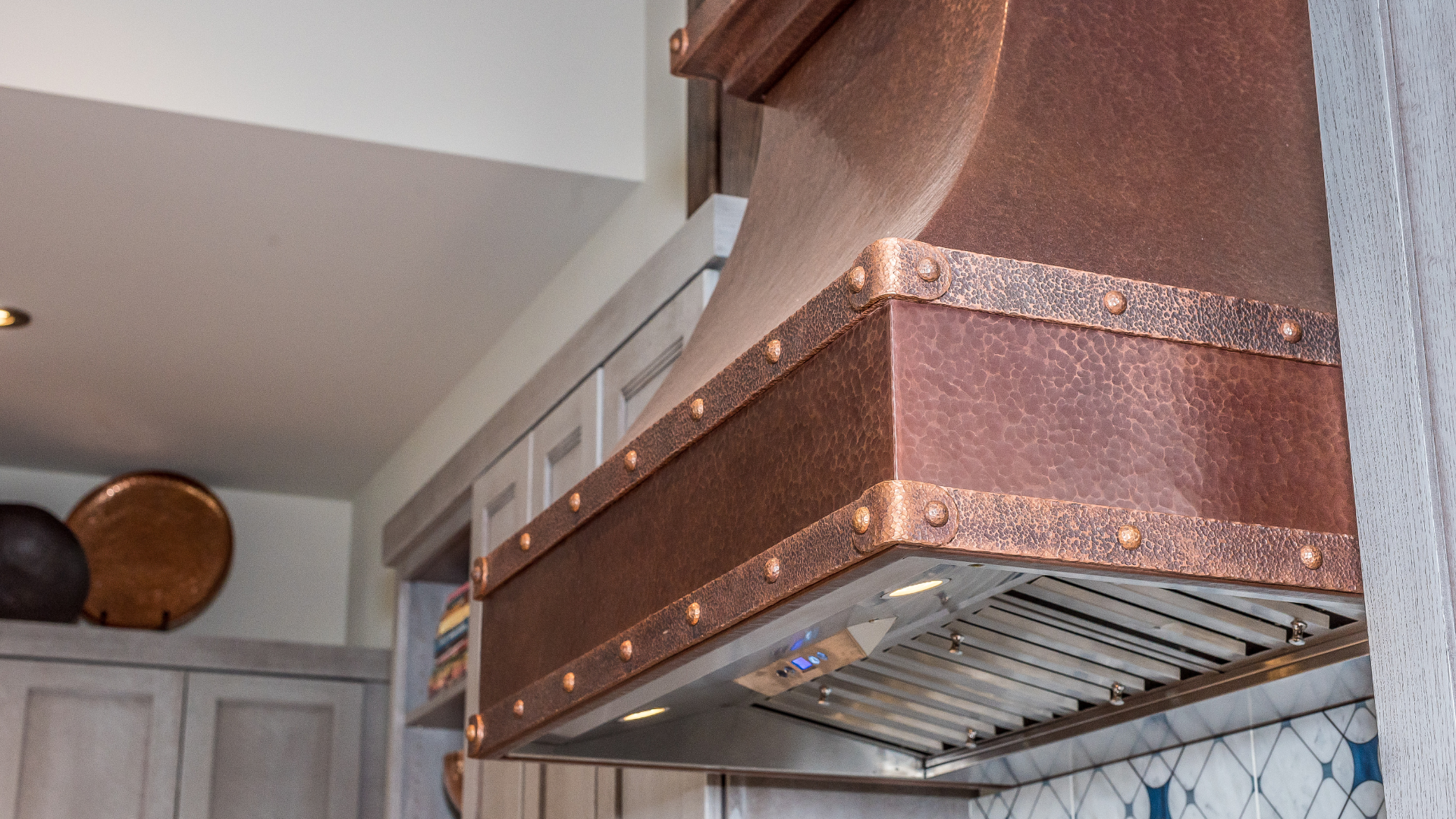 A copper hood is hanging from the ceiling in a kitchen.