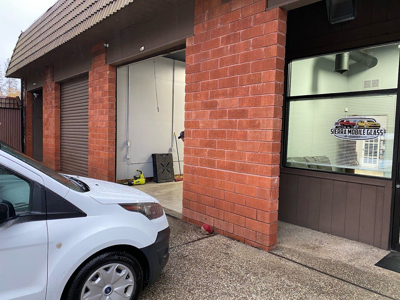 Semi & fleet windshield replacement in Truckee & Grass Valley, CA Brick garage with open bay, silver car parked outside, and storefront window beside a wet driveway