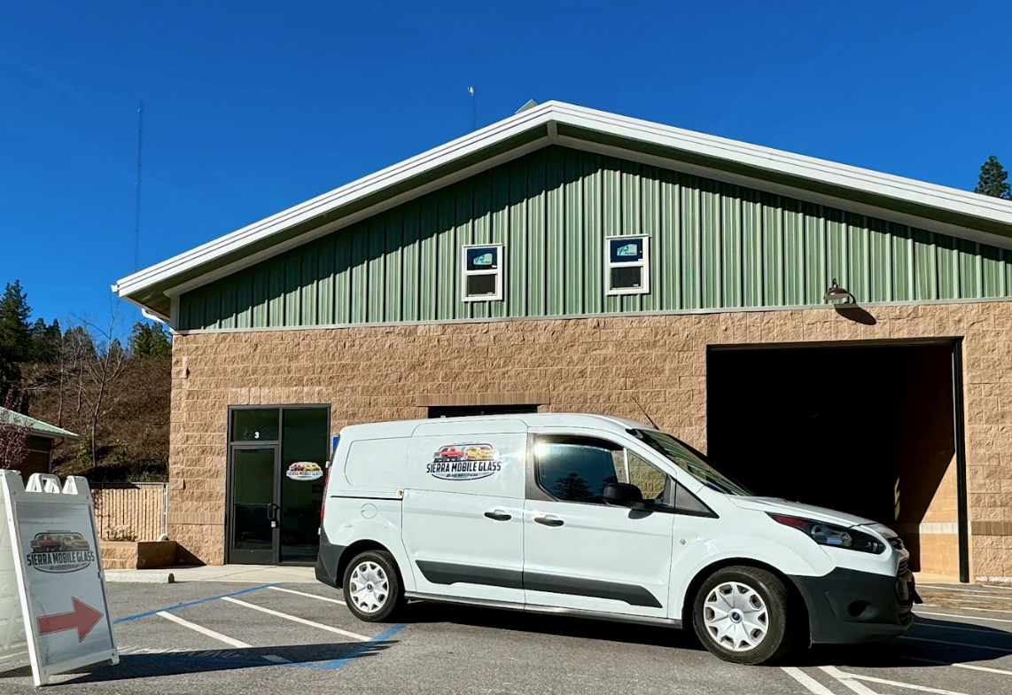 BMW Windshield replacement in Truckee, CA White service van parked outside a green building with an open garage bay under a blue sky