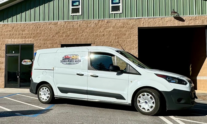 White cargo van parked outside a tan building with green siding, next to an open garage bay.