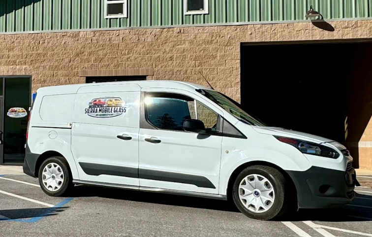 White service van parked outside a beige building with a green upper facade and an open garage bay.