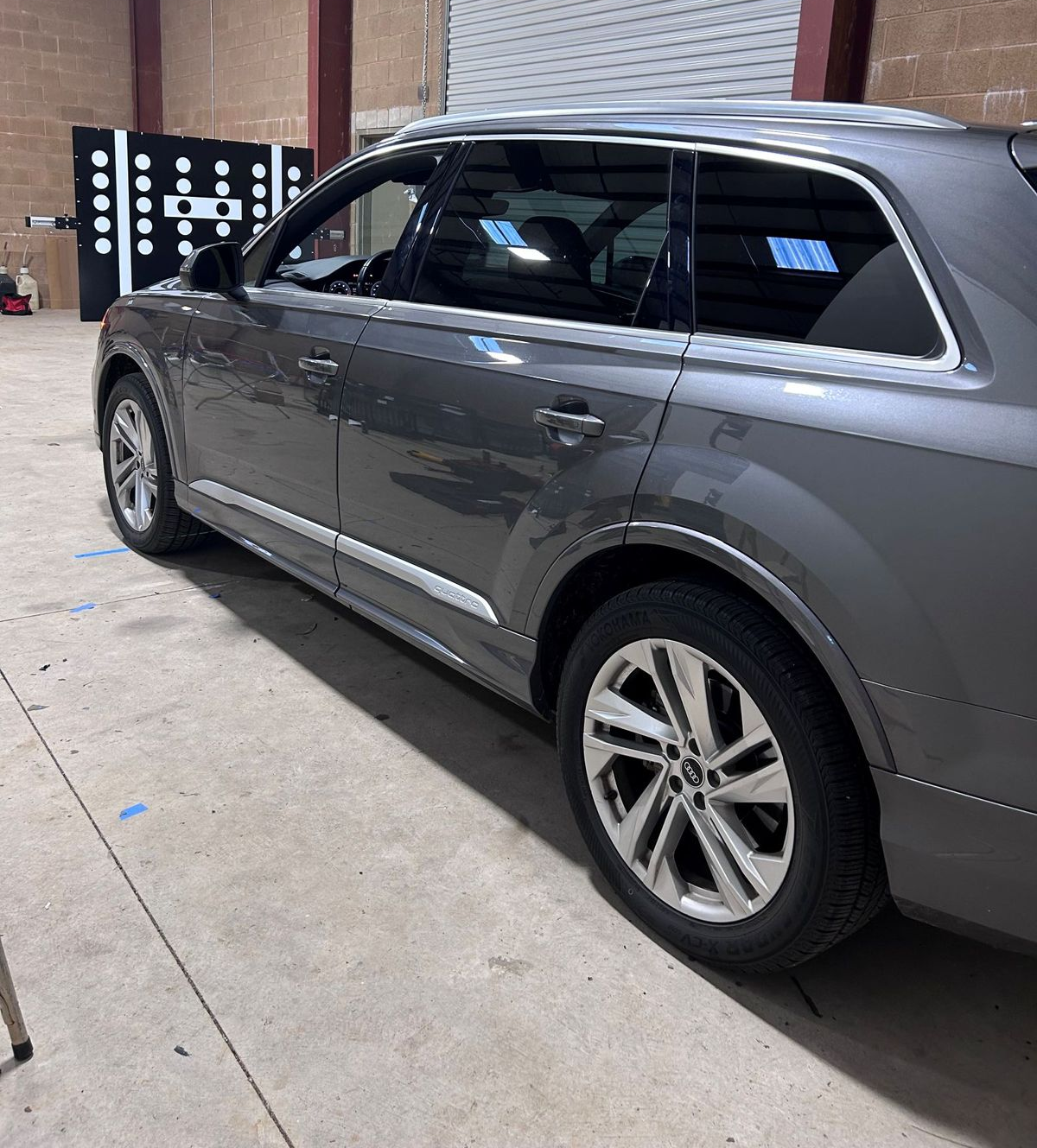 Gray SUV parked indoors near a brick wall and concrete floor, viewed from the side.