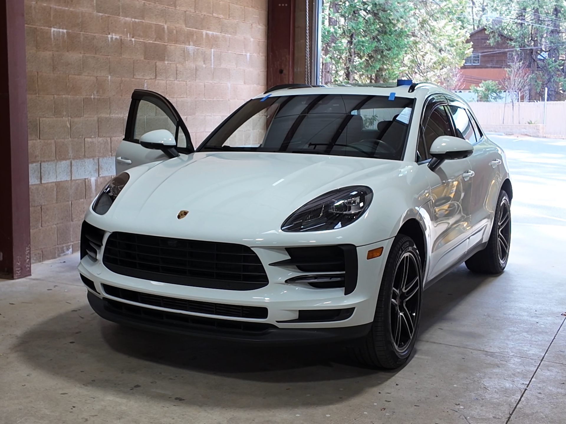 White Porsche SUV parked under a covered driveway with the driver’s door open