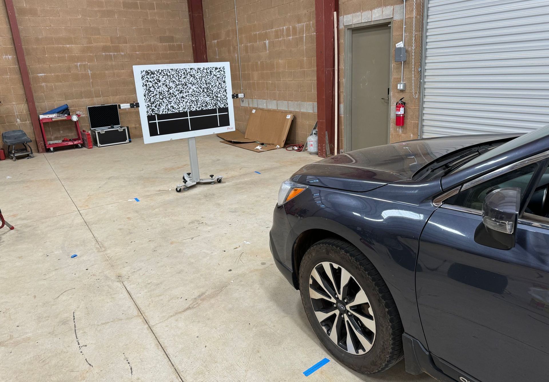 ADAS windshield calibration in Truckee & Grass Valley, CA Warehouse interior with a black car in the foreground and a target board on a stand in the background.