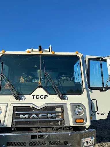 Front view of a white Mack truck cab against a blue sky, with the driver door open.