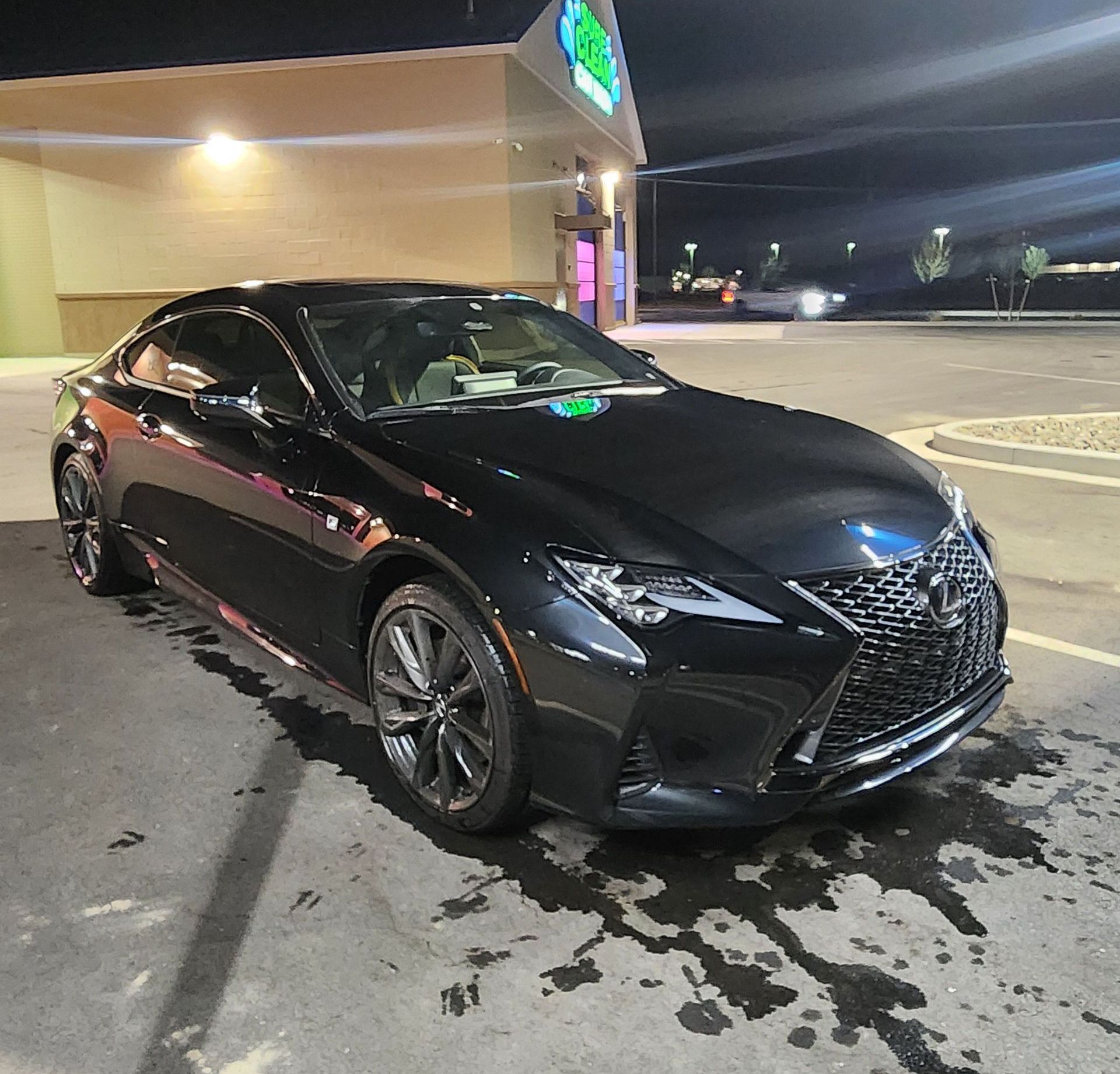 Lexus ADAS Calibration in Truckee, CA Black Lexus sedan parked at night outside a lit storefront, with wet pavement reflections.