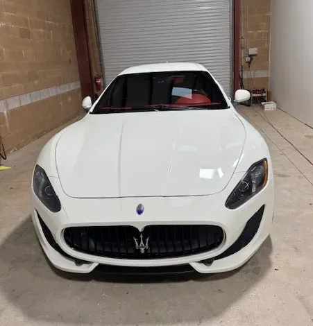 Maserati auto glass replacement in Grass Valley, CA White sports car parked indoors in a garage, front view with a Maserati grille and logo.