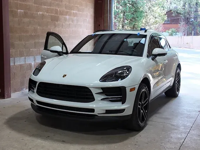 White Porsche SUV parked in a covered garage with the driver's door open